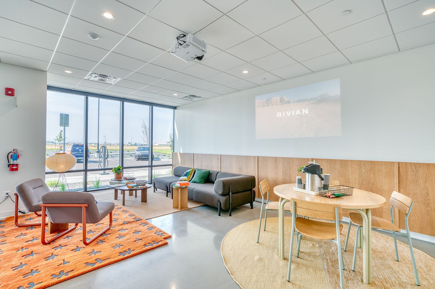 Modern lounge with seating, window, projector screen showing text, and round dining table.