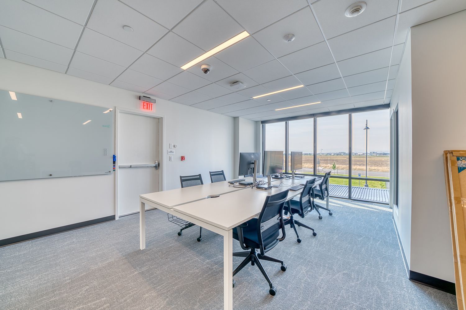 Conference room with white tables, black chairs, and large windows overlooking a distant view.