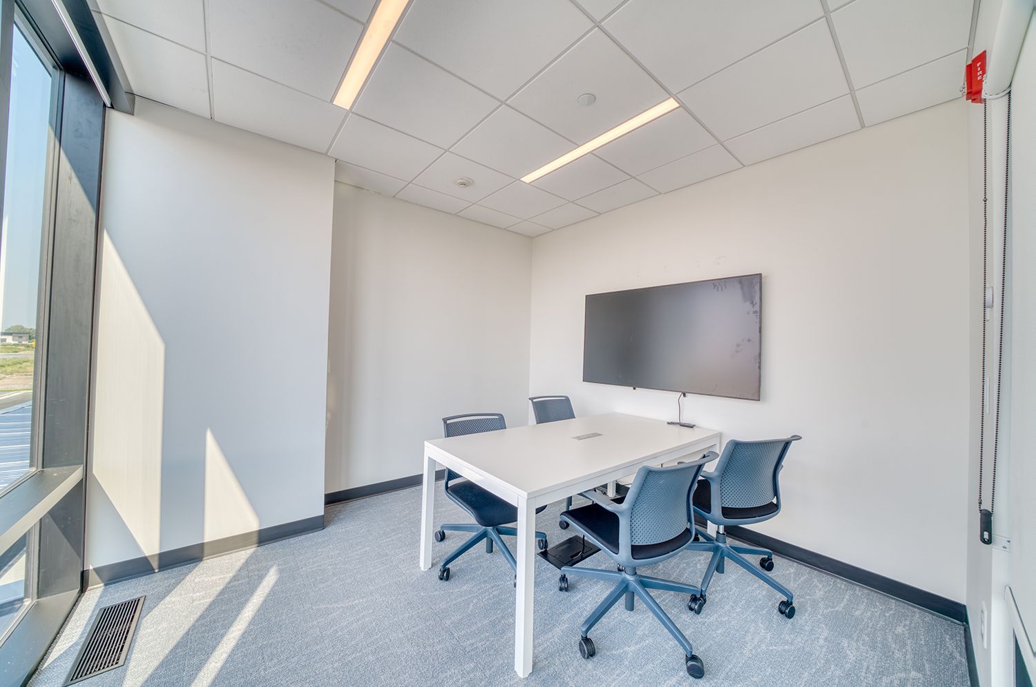 Small, bright conference room with table, chairs, TV, and large window.