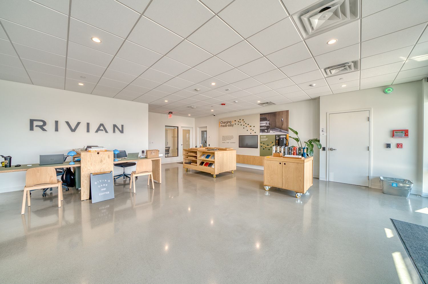 Bright Rivian office interior with logo, light wood furniture, and a polished concrete floor.