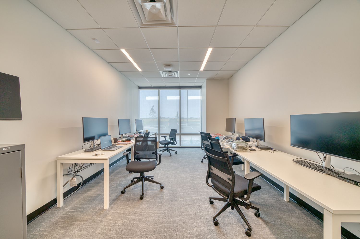 Office room with white desks, computers, and black chairs. Window and ceiling lights.