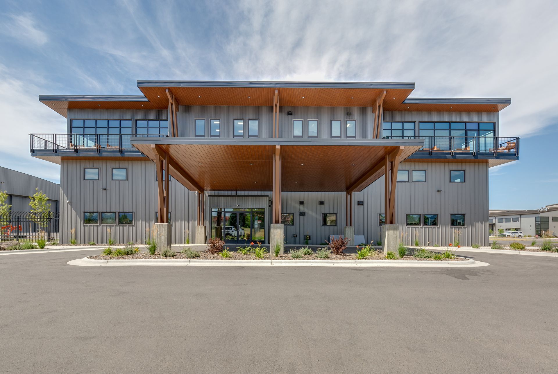 Modern two-story building with a covered entrance, wood accents, and large windows under a blue sky.