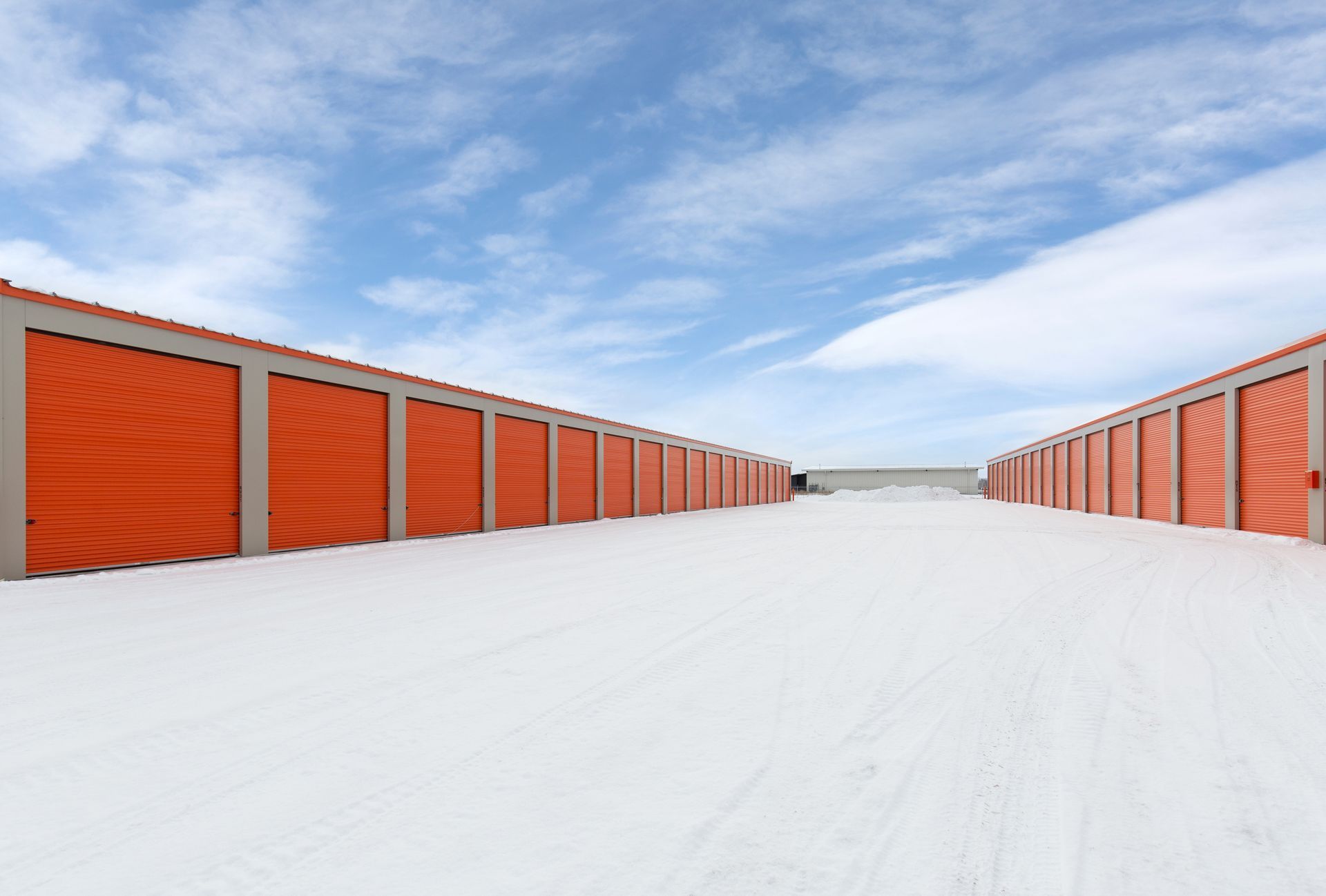 Storage units with orange doors under a blue cloudy sky.