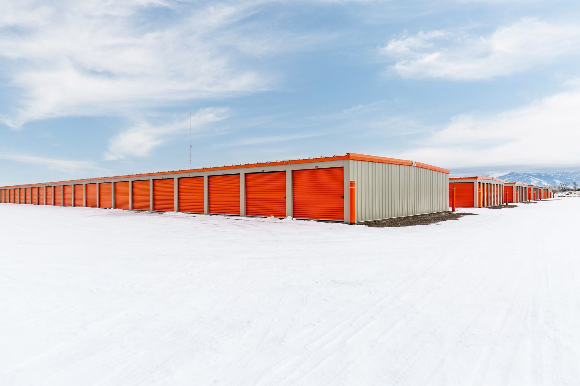 Row of orange storage units in snow under a partly cloudy sky.