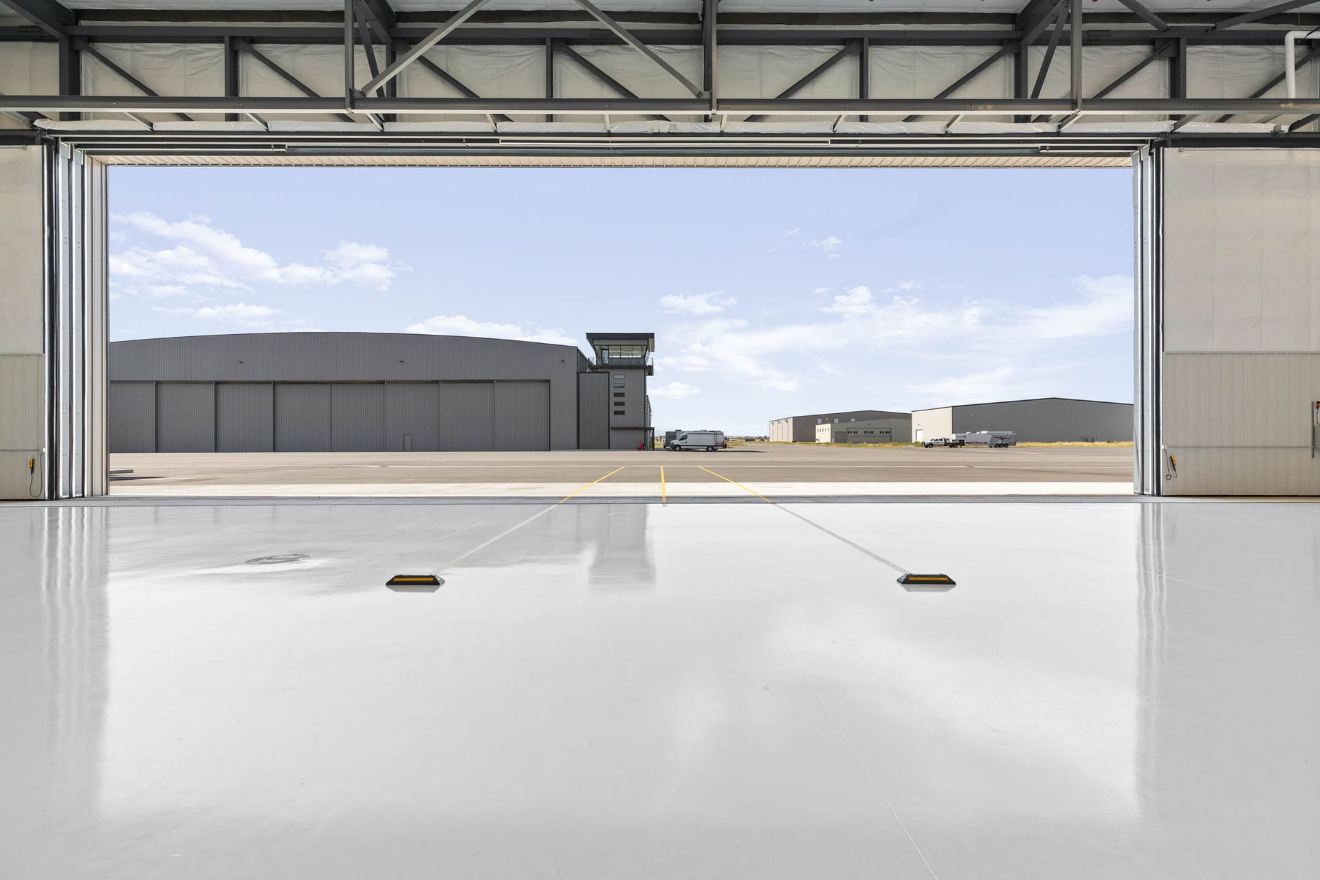 View from inside a large hangar, looking out to an airfield and buildings under a blue sky.