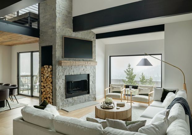 Living room with fireplace, white sectional sofa, large windows, and a view of trees.