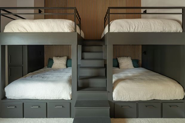 Two connected bunk bed sets with gray frames, steps, and storage drawers. Each bed has white bedding and a green pillow.