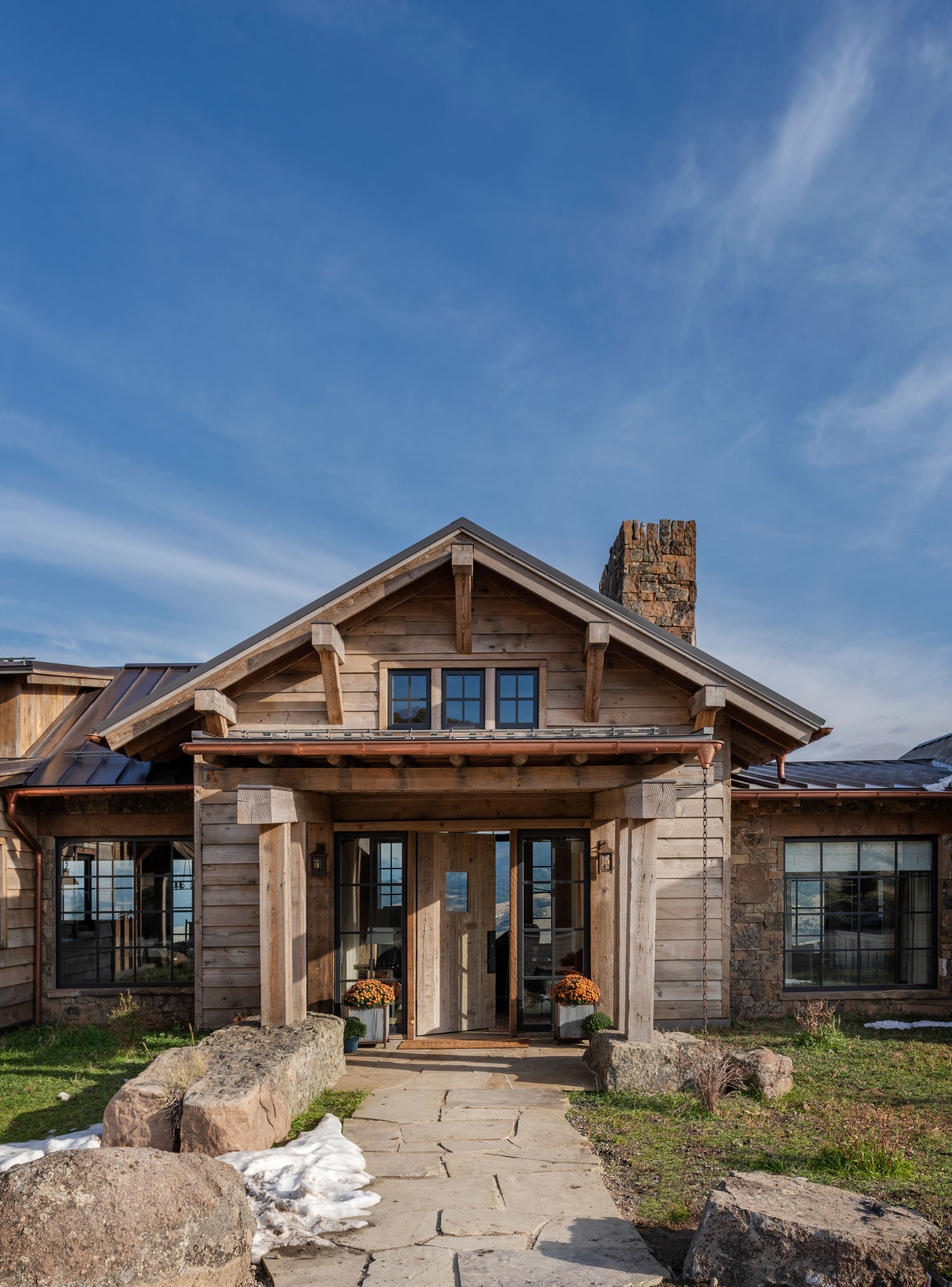 Rustic wooden lodge with stone facade and walkway, under a blue sky.