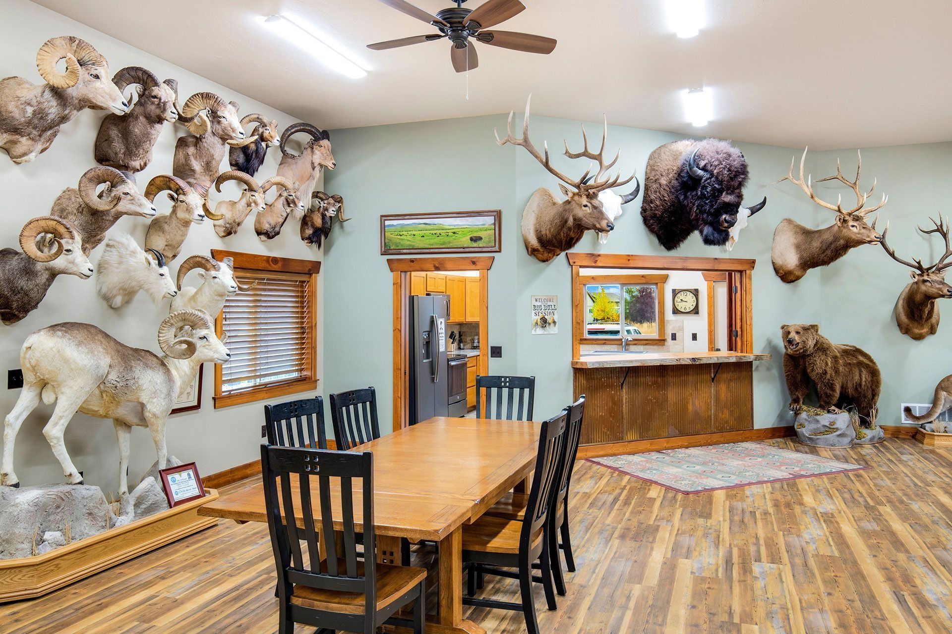 Hunting lodge dining room with taxidermied animal heads on walls, wooden table, chairs, and bar.
