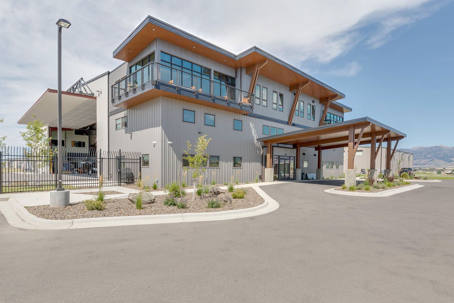 A modern, gray commercial building with a wooden covered entrance and large windows, situated on a paved lot