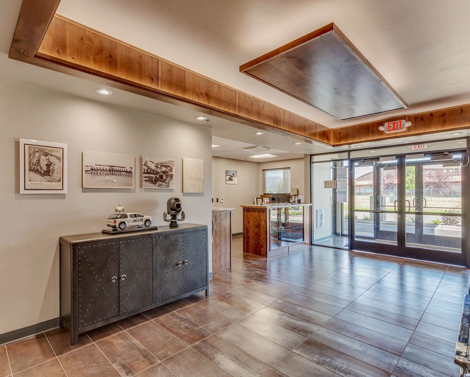 A hotel or office lobby features a dark metal console table with art on the walls, a wooden reception desk, and glass doors