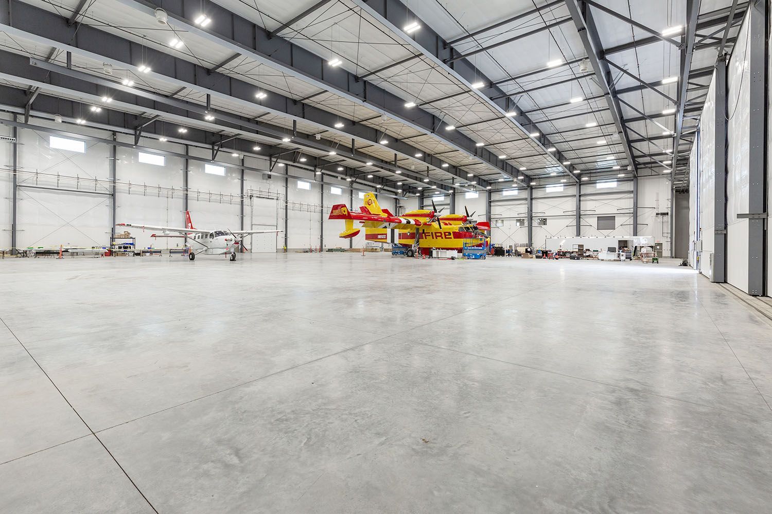 A bright, spacious airplane hangar with a concrete floor, housing a red and yellow firefighting aircraft