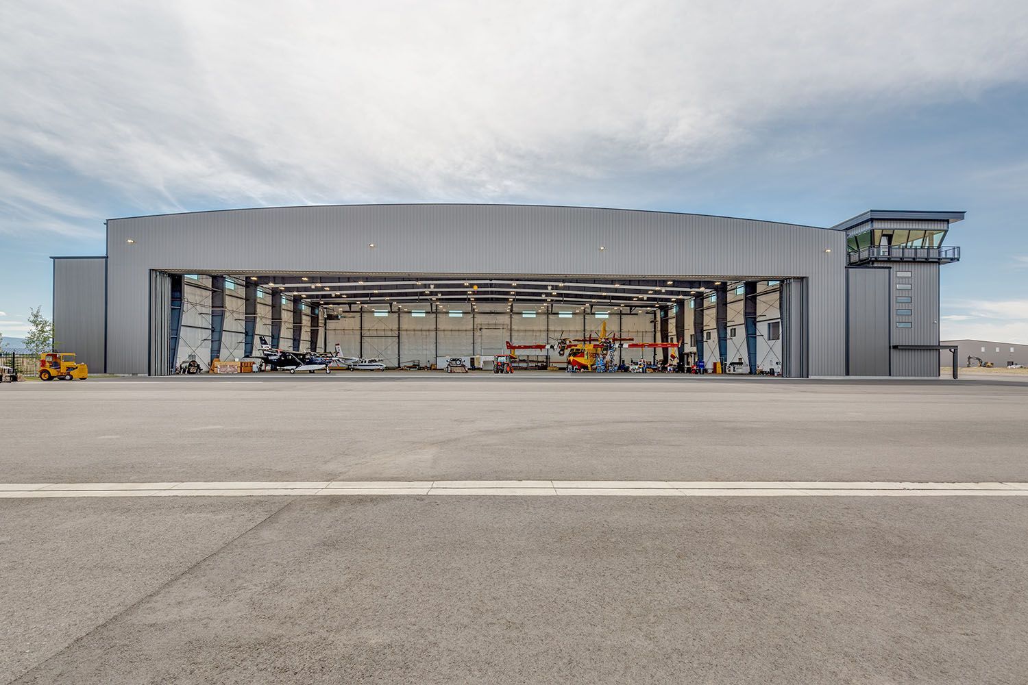 A large, gray industrial hangar with a side observation tower under a cloudy sky on a paved airfield