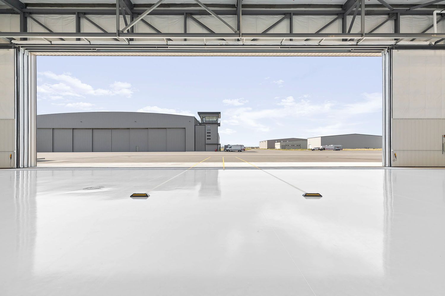 A view from inside a brightly lit hangar, looking out toward an airfield with metal buildings