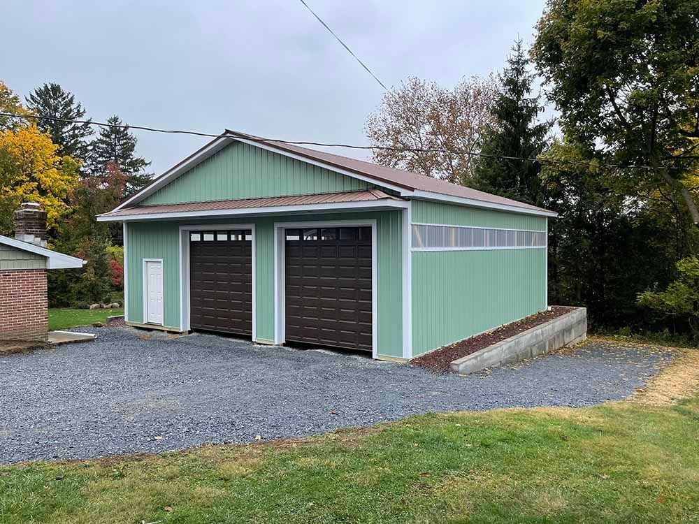 A green garage with two garage doors is sitting on top of a gravel driveway.