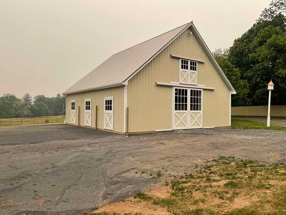 A large barn with white doors is sitting in the middle of a field.