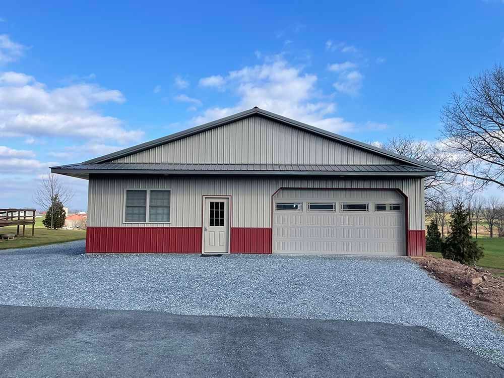 A garage with a red and white trim is sitting on top of a gravel driveway.