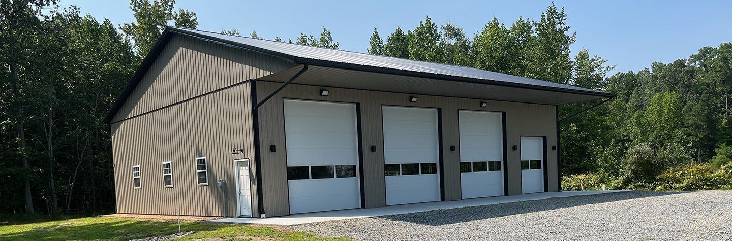 A large garage with three white garage doors is sitting on top of a gravel road.