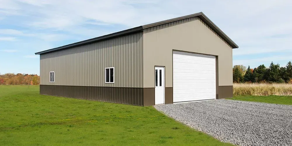 A large metal building with a white garage door is sitting in the middle of a grassy field.