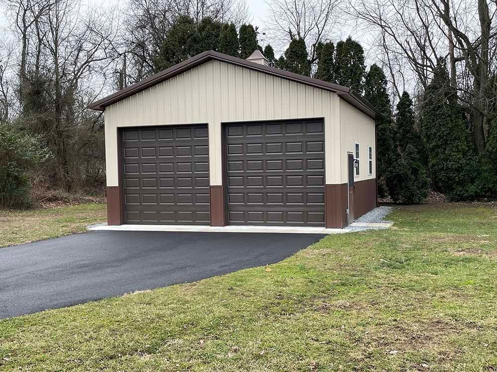 A garage with two garage doors is sitting in the middle of a grassy field.