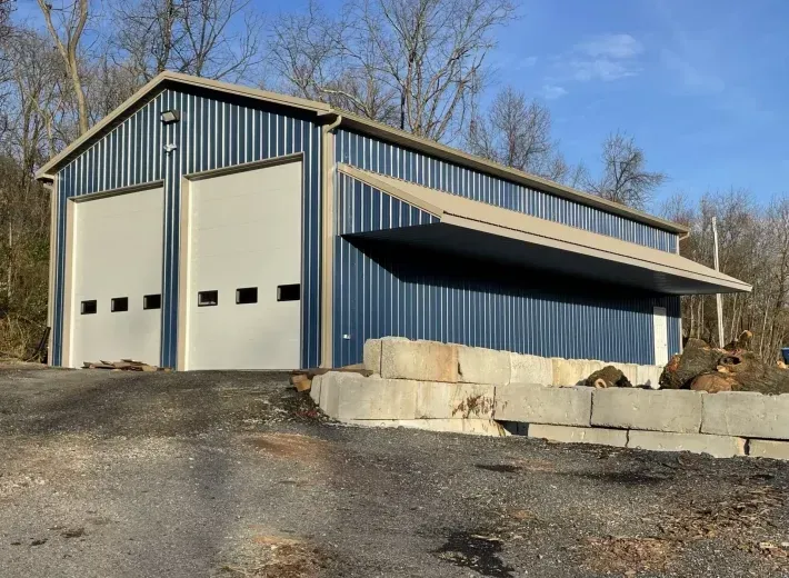 A large metal building with two garage doors is sitting on top of a dirt hill.