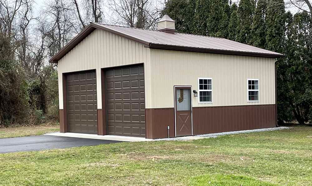 A garage with two garage doors is sitting in the middle of a grassy field.