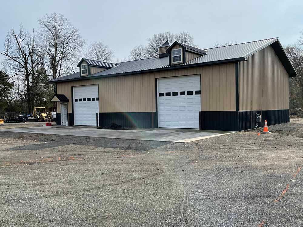 A large building with two garage doors is sitting on top of a dirt field.