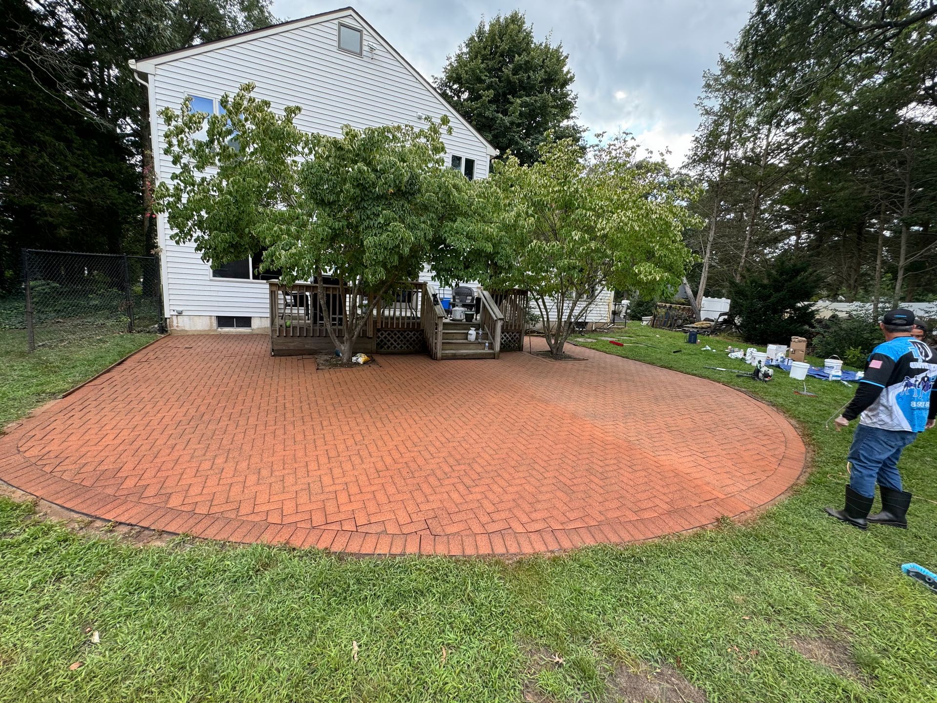 A man is cleaning a brick patio in front of a house.