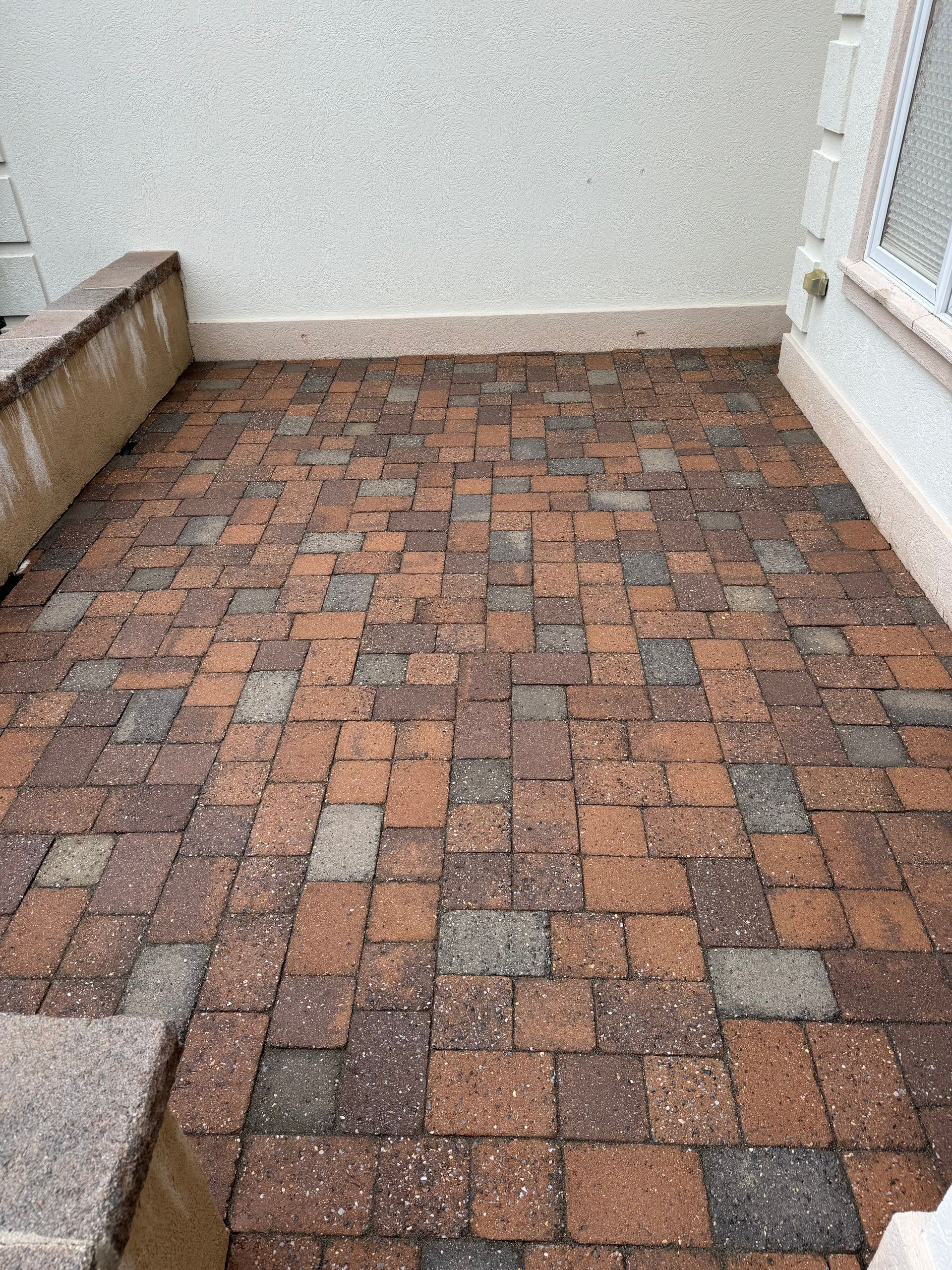 A brick patio with a white wall and a window in the background.