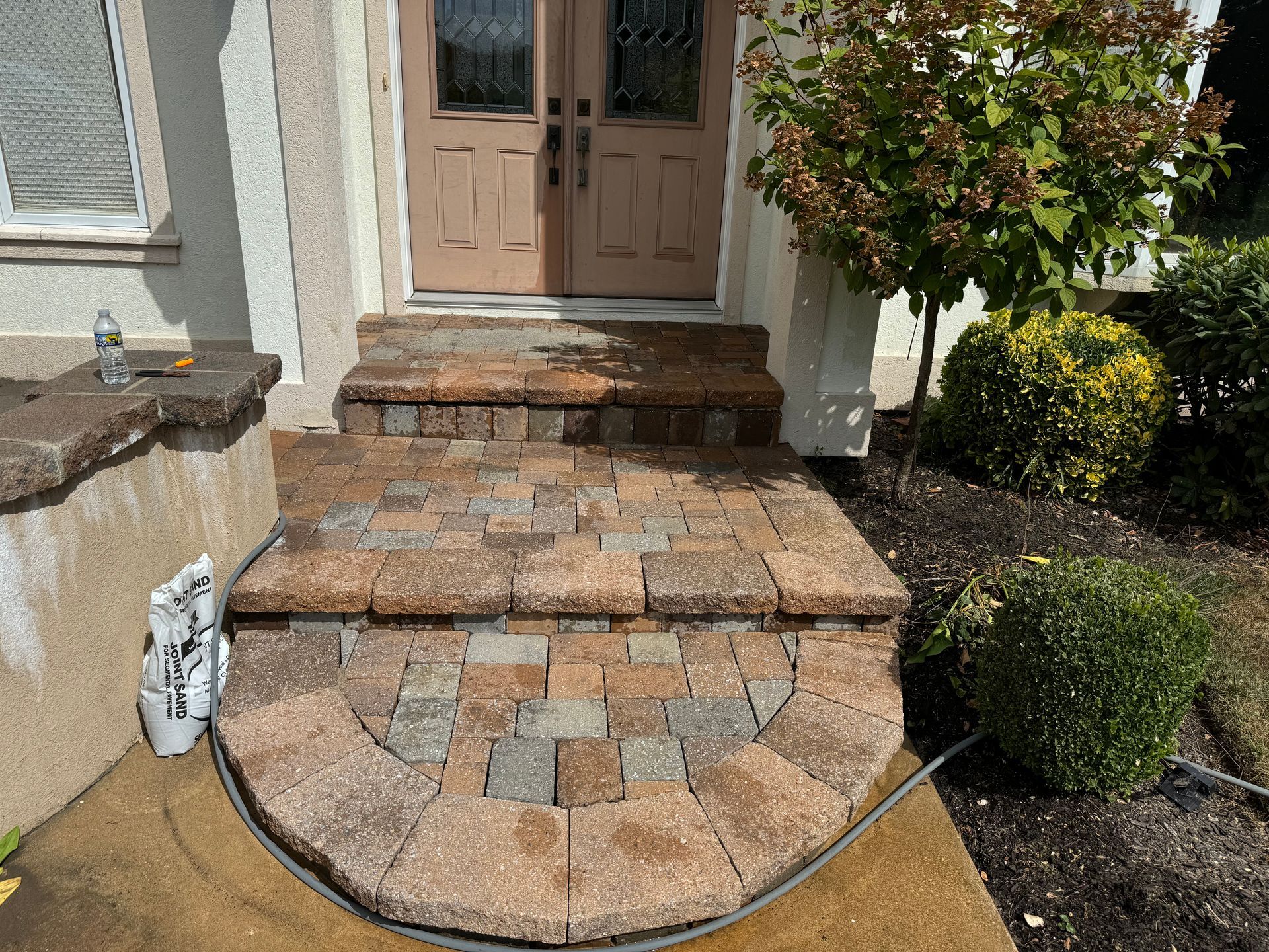 A hose is connected to a brick walkway in front of a house.