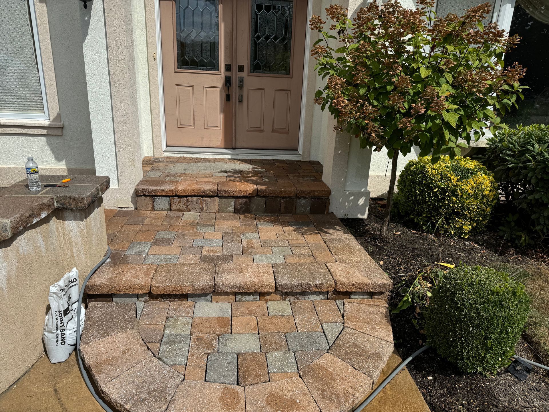 A hose is connected to a brick walkway in front of a house.