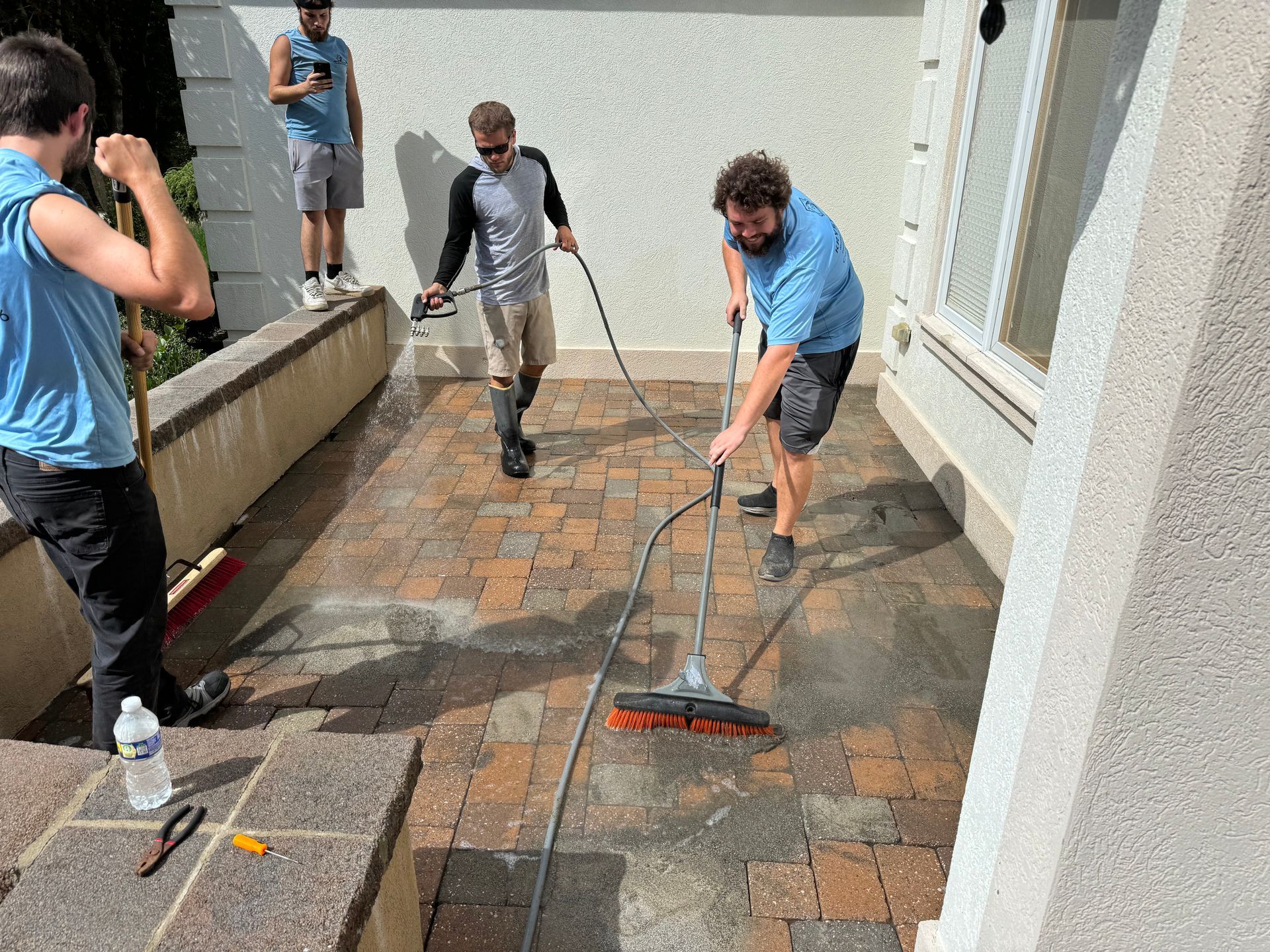 A group of men are cleaning a brick patio with a broom.