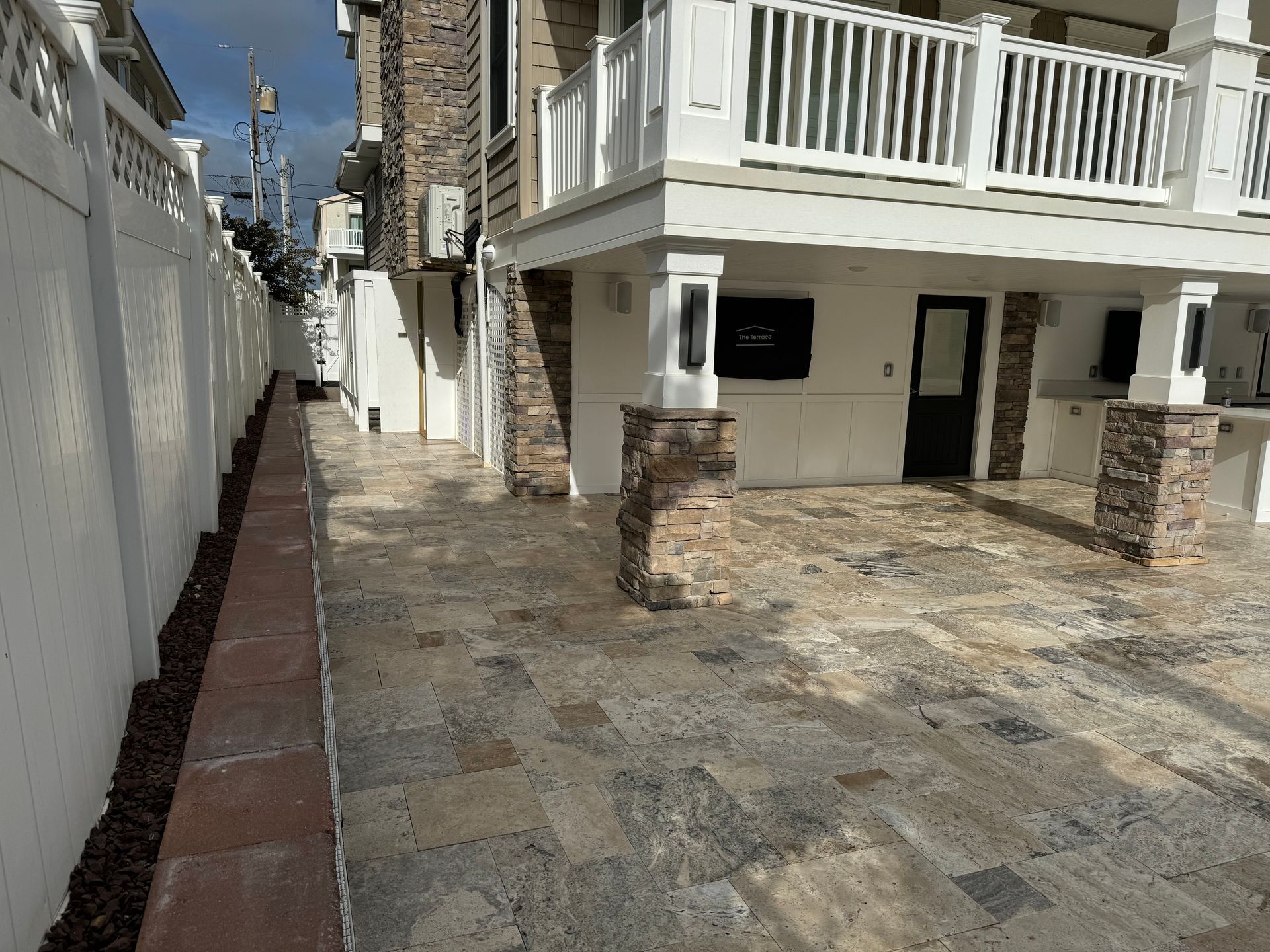 A brick walkway leading to a white house with a balcony