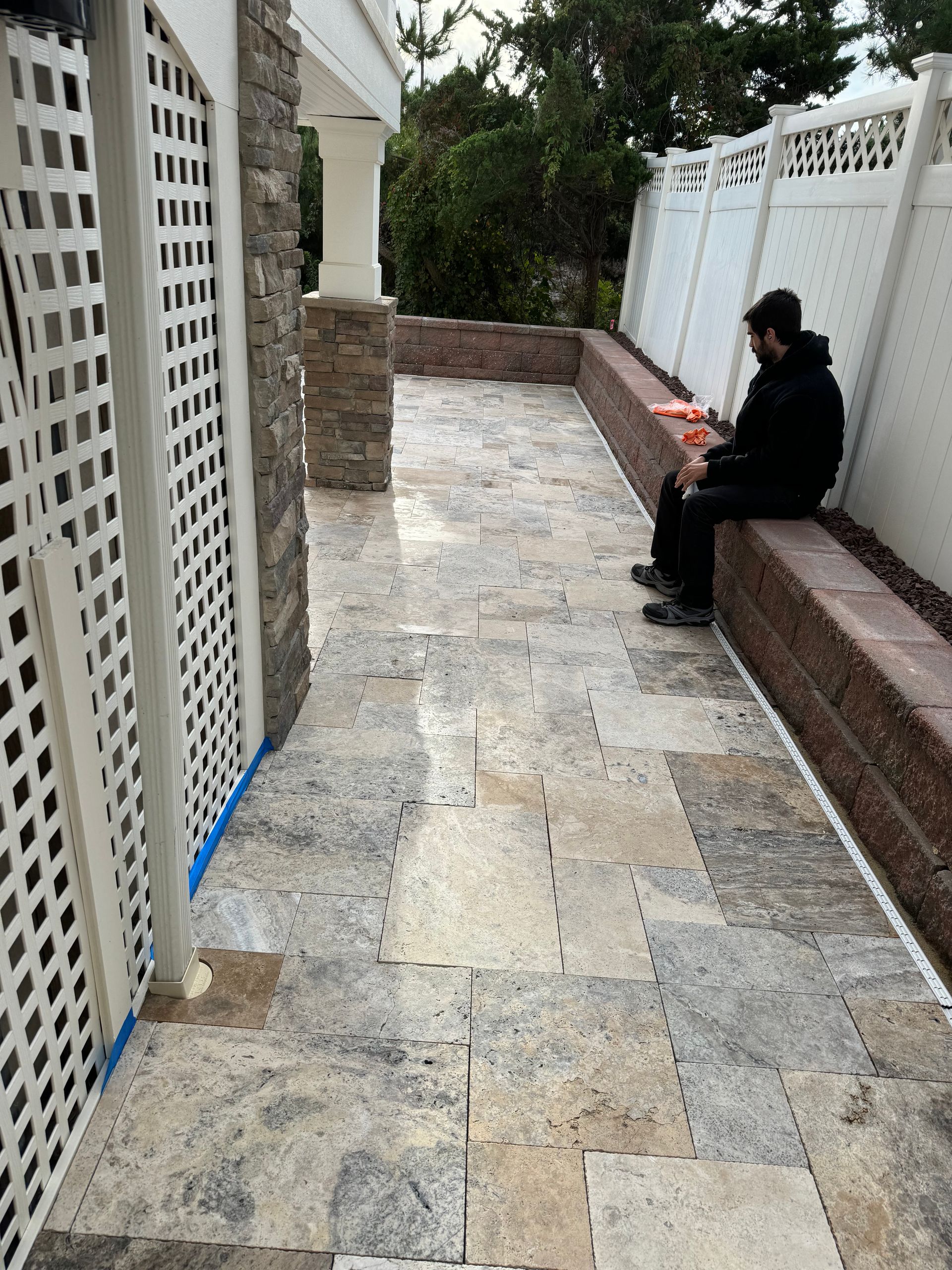 A man is sitting on a bench on a sidewalk next to a fence.