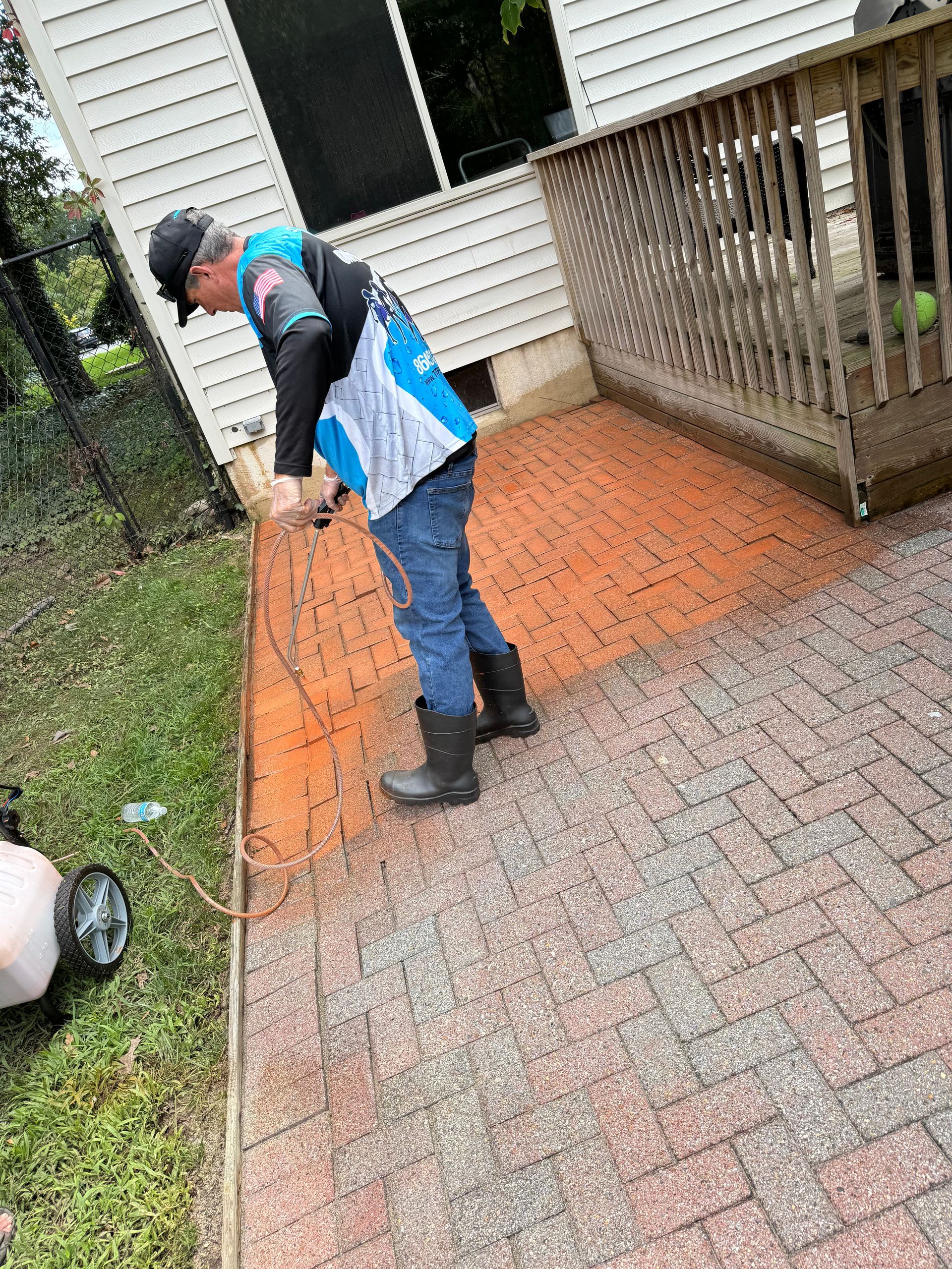 A man is cleaning a brick walkway with a sprayer.