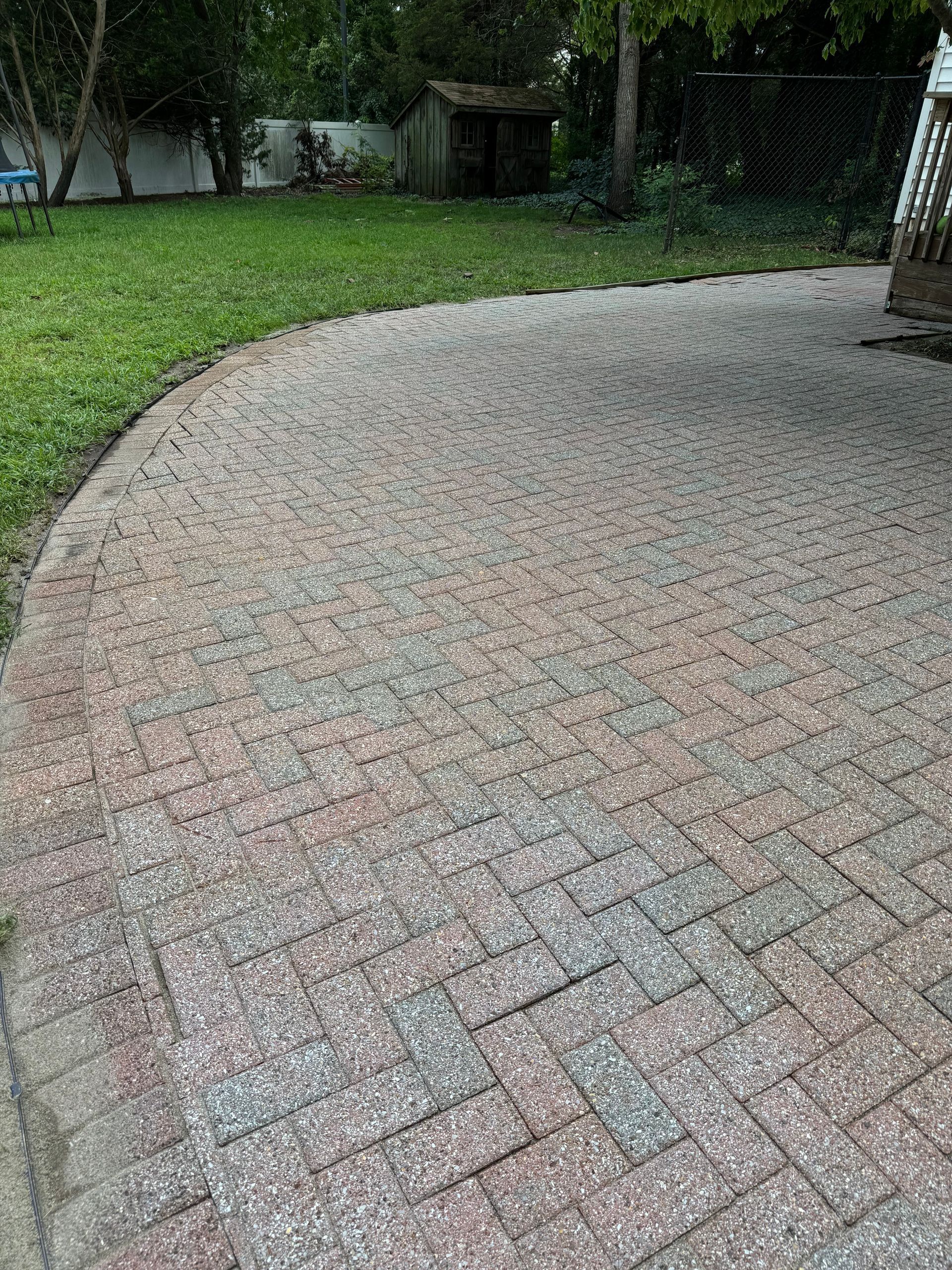 A brick patio in a backyard with a shed in the background.