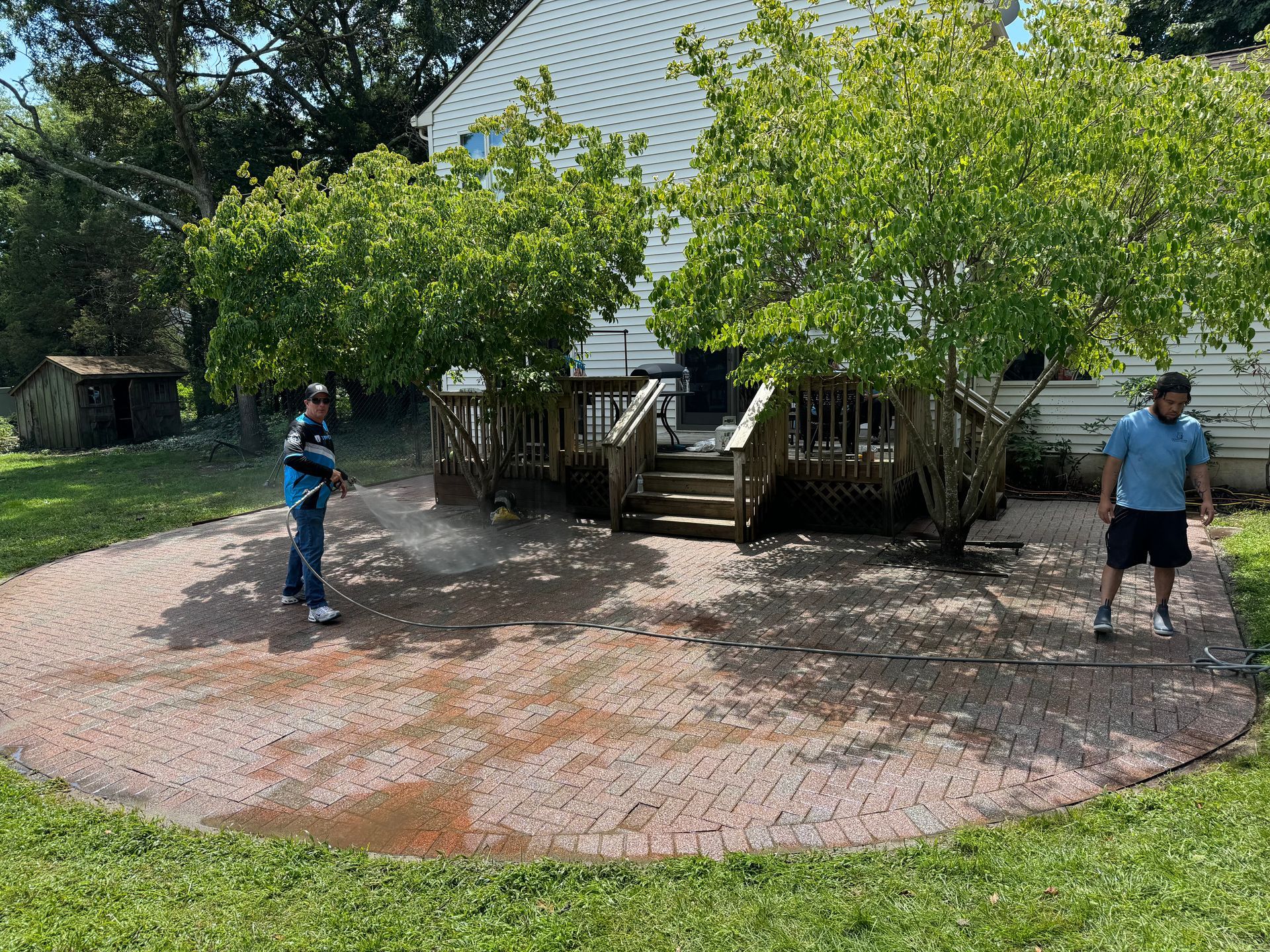 Two men are cleaning a brick patio in front of a house.