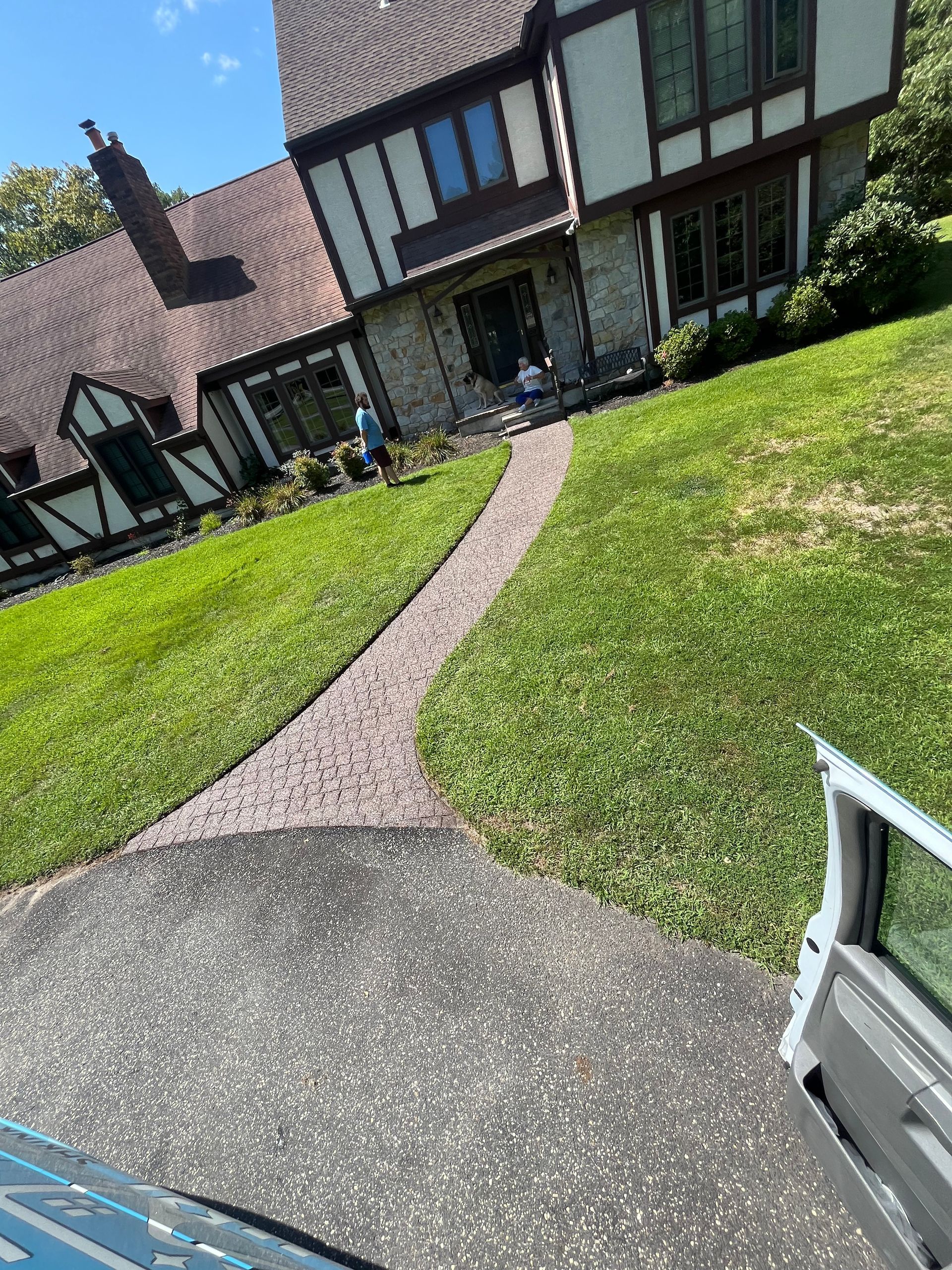 A car is parked in front of a house with a path leading to it.