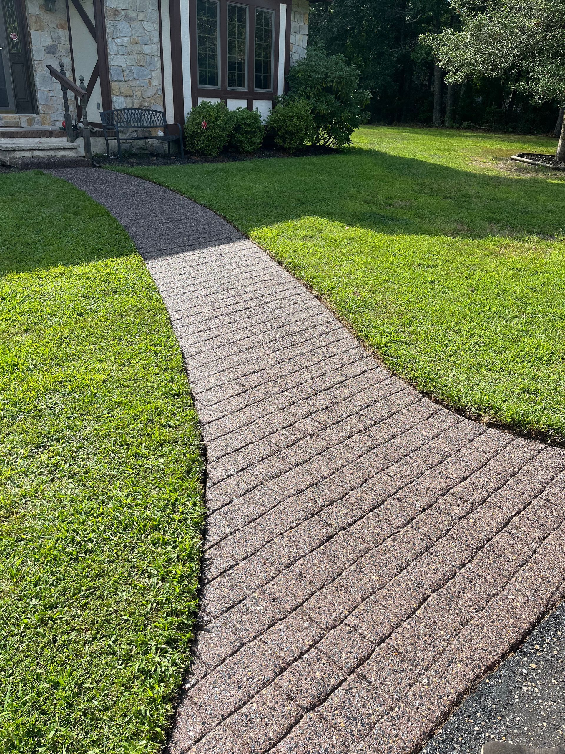 A brick walkway leading to a house in a lush green yard.