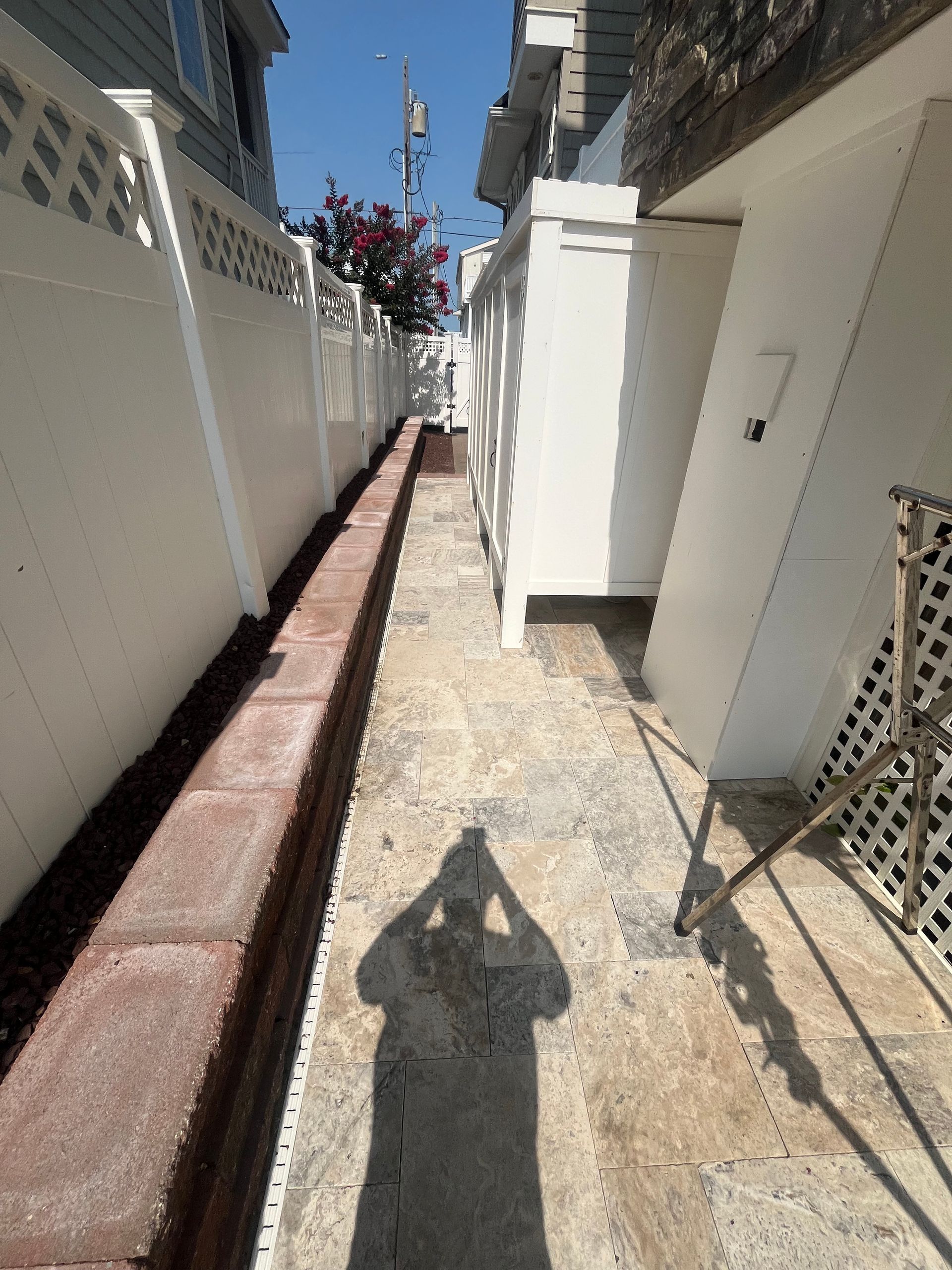 A shadow of a person is cast on a sidewalk next to a white fence.