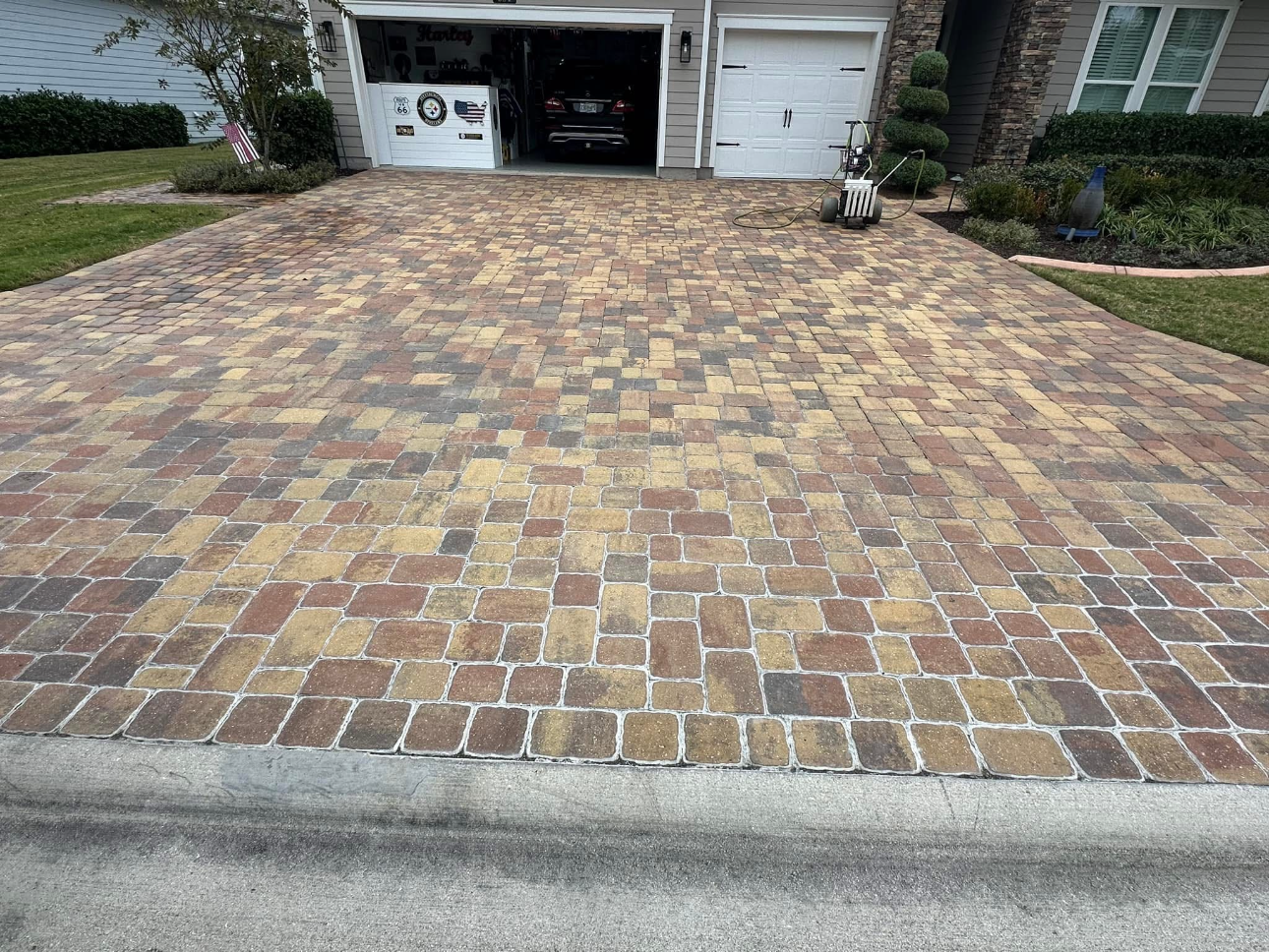 A brick driveway in front of a house with a car parked in the garage.