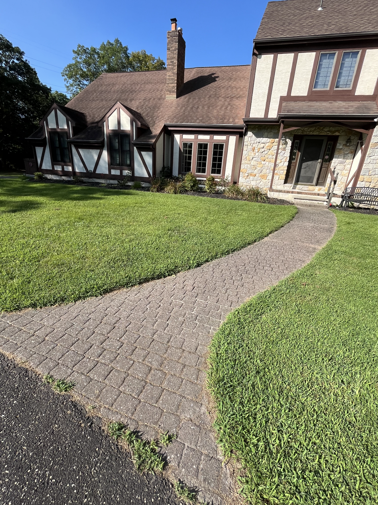 A house with a brick walkway leading to it and a lush green lawn.