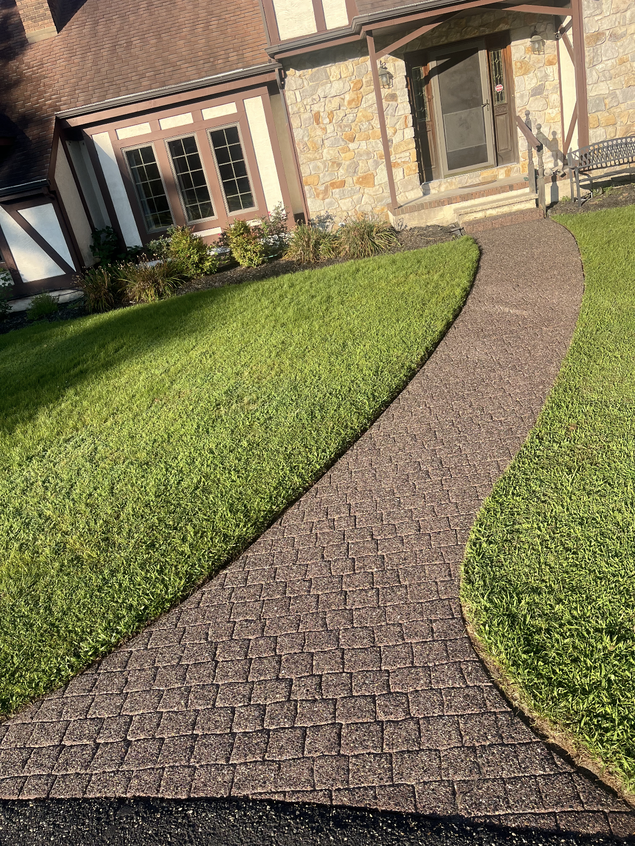 A walkway leading to a house with a lush green lawn.