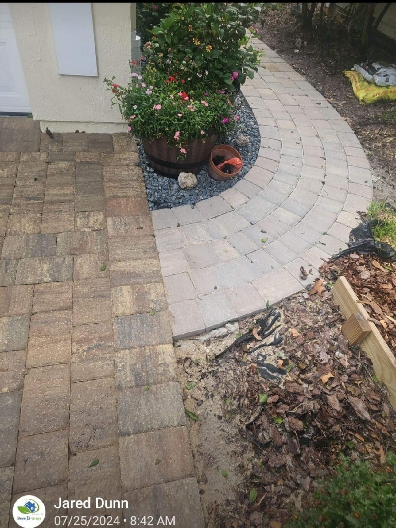 A brick walkway leading to a house with flowers in pots.