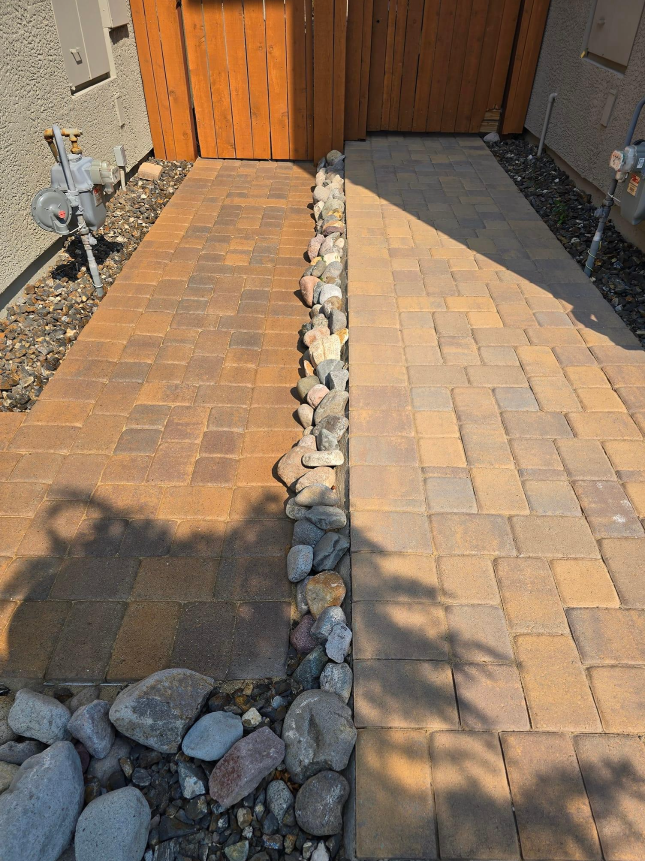 A brick walkway with rocks on the side and a wooden gate in the background.