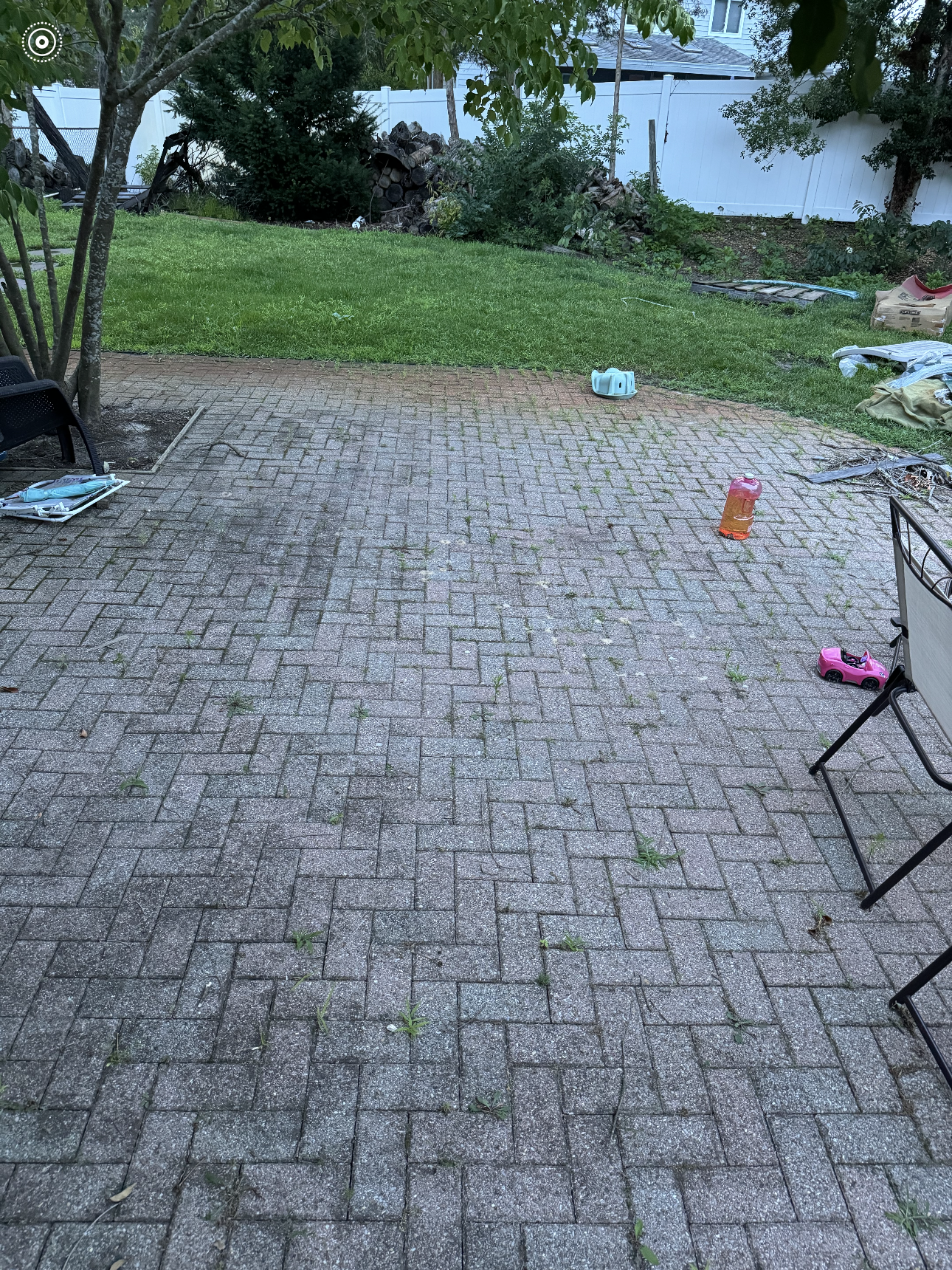 A brick patio with a chair and a tree in the background.