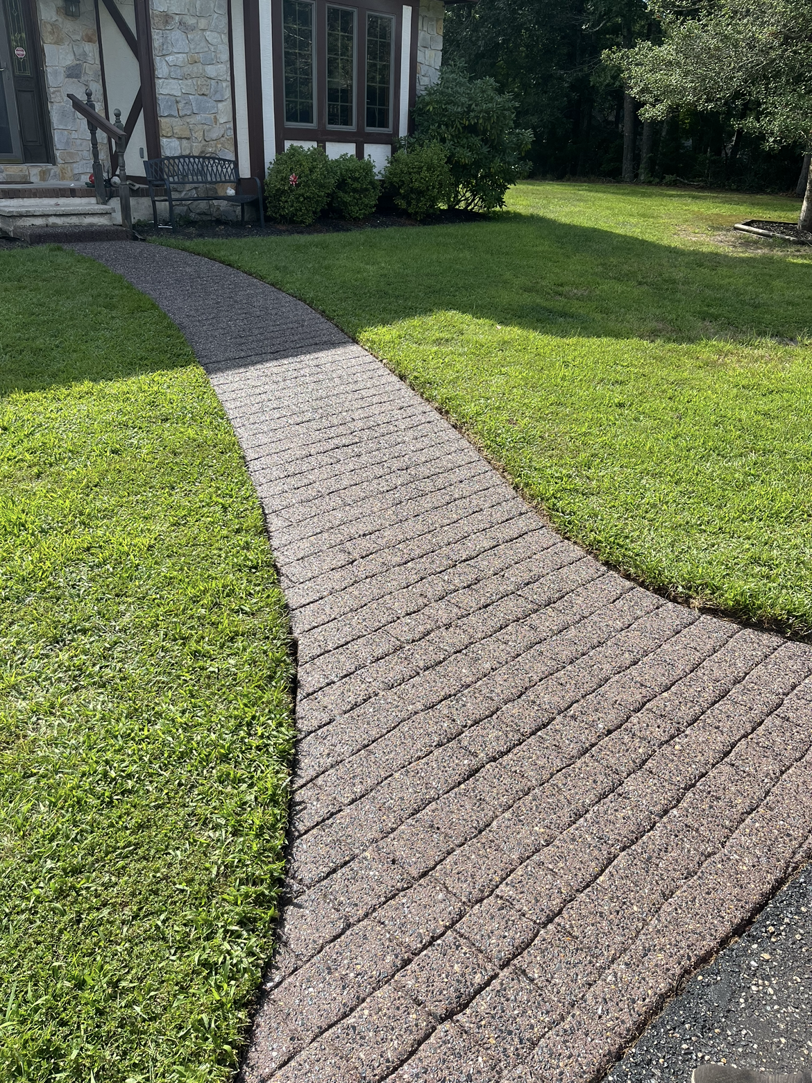 A brick walkway leading to a house with a lush green lawn.