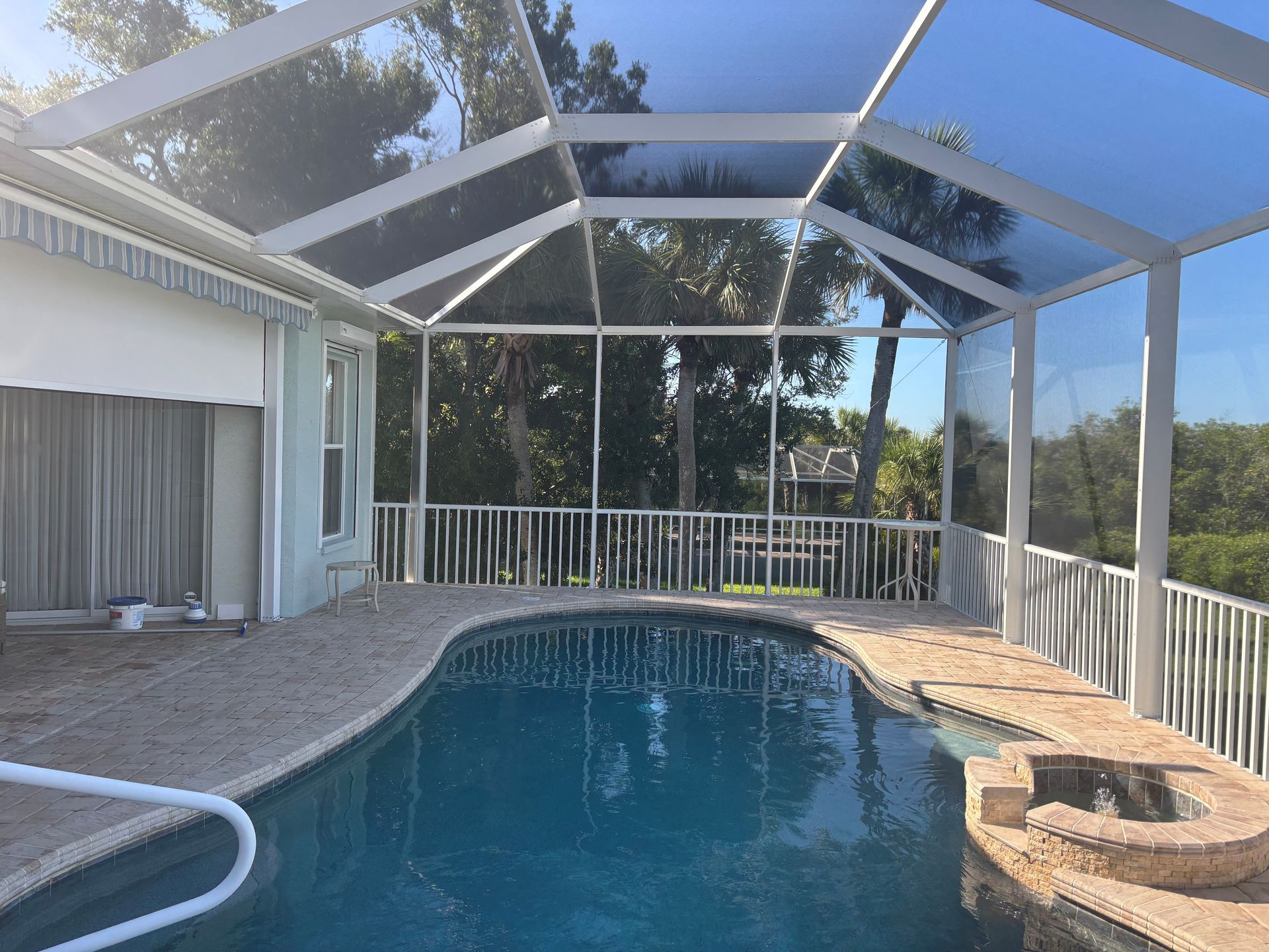 Screened-in pool area with a swimming pool, white railing, and a view of trees under a blue sky.
