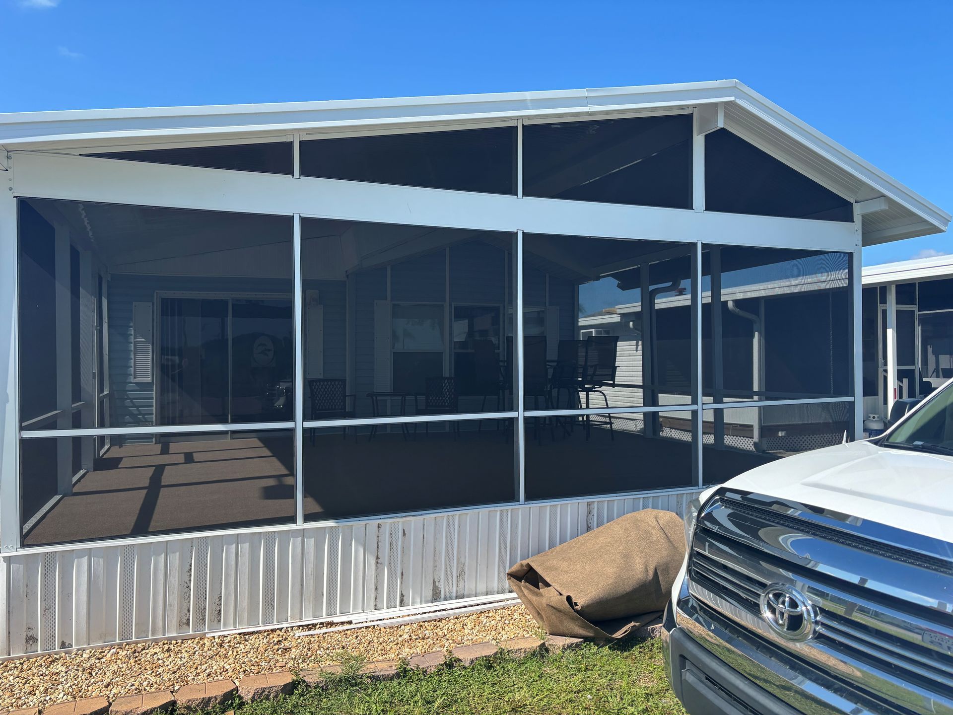 Screened porch extension on a mobile home with a white frame and dark screens under a blue sky.