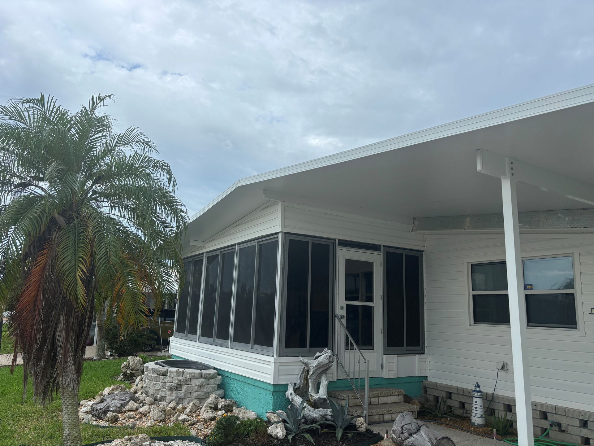 White house with screened porch, palm tree, and cloudy sky.